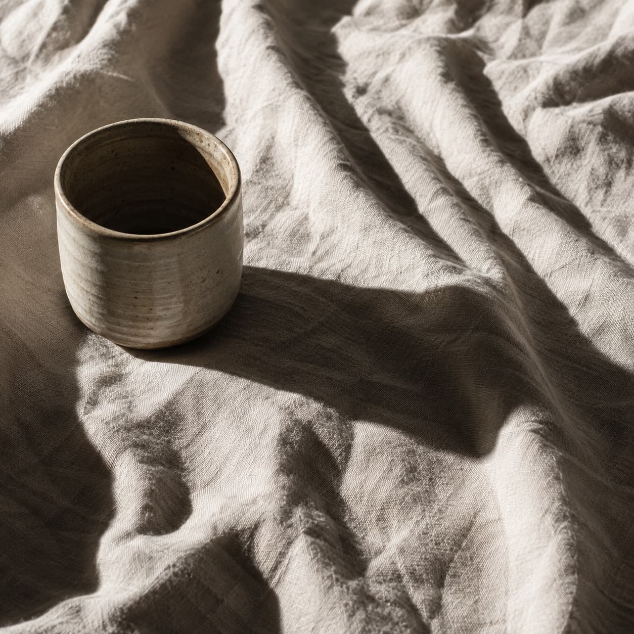 Close detail of rumpled undyed linen beside a single ceramic cup.