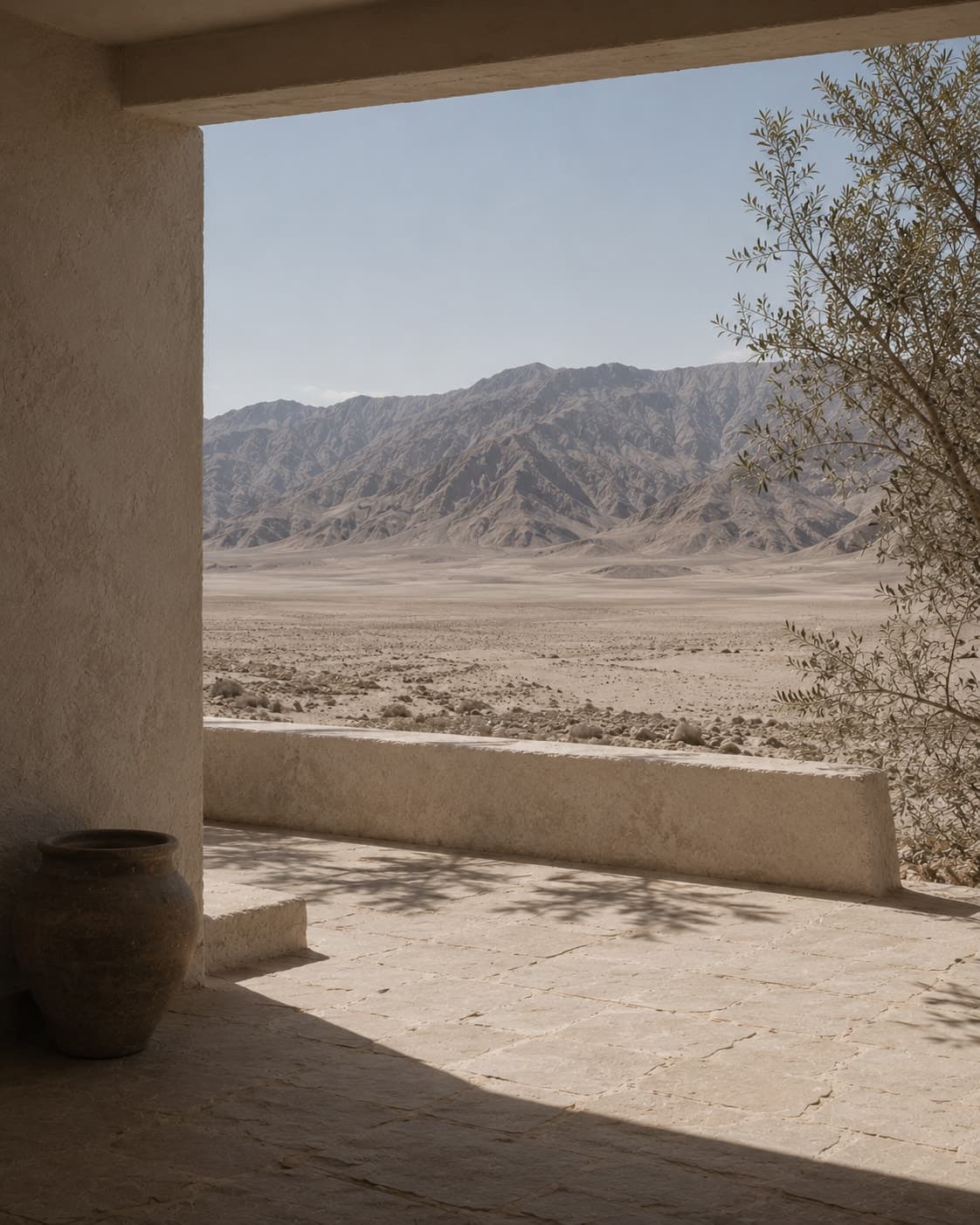 A covered terrace off a guest room, a low plaster wall at its edge, pale flagstone underfoot, and the far wall of the basin forty kilometres out under a bleached sky.
