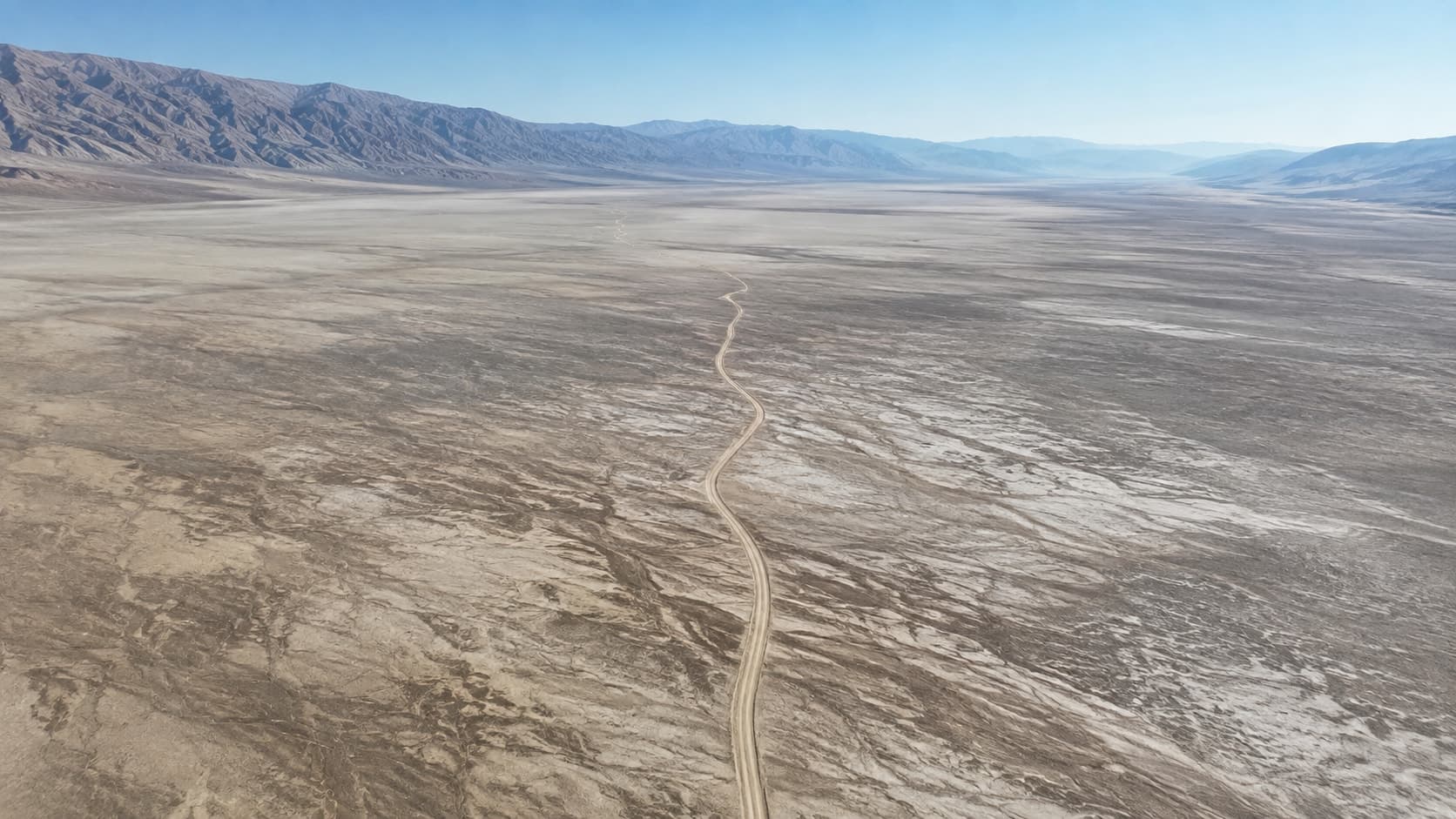 An oblique aerial view of a single dirt track threading an otherwise empty basin.